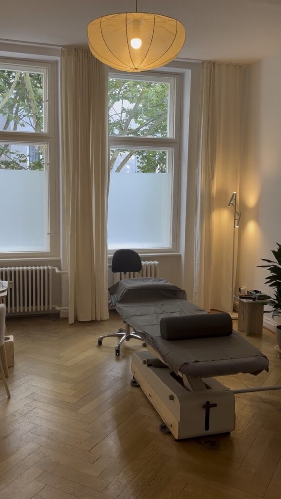 Behandlungsraum mit Liege und hohen Altbaufenstern